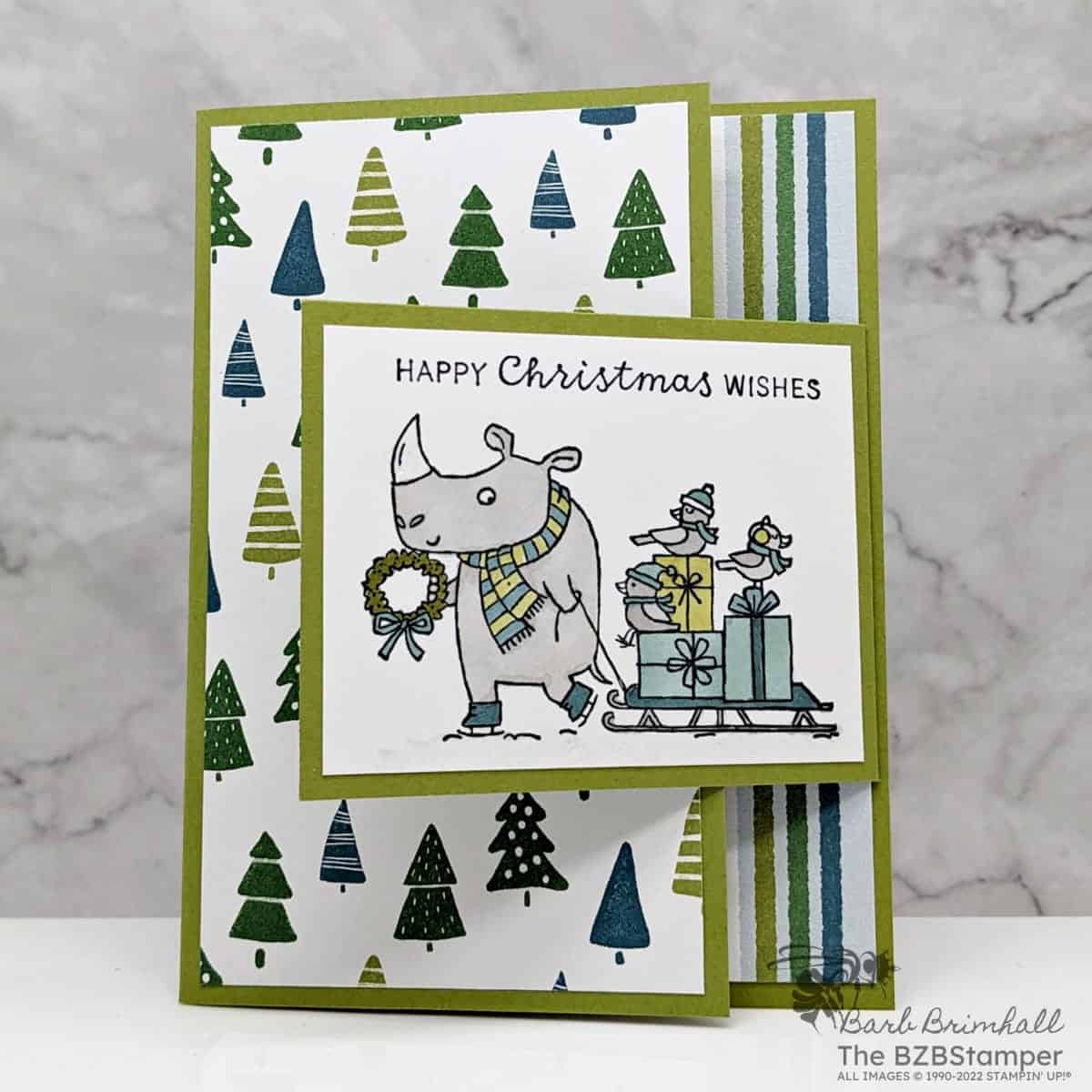 Christmas Card with the Festive and Fun Stamp Set 1 Christmas card with the Festive and Fun Stamp Set by Stampin' Up! in greens and blues featuring a rhino pulling a sled with birds and presents and sentiment "Happy Christmas Wishes."