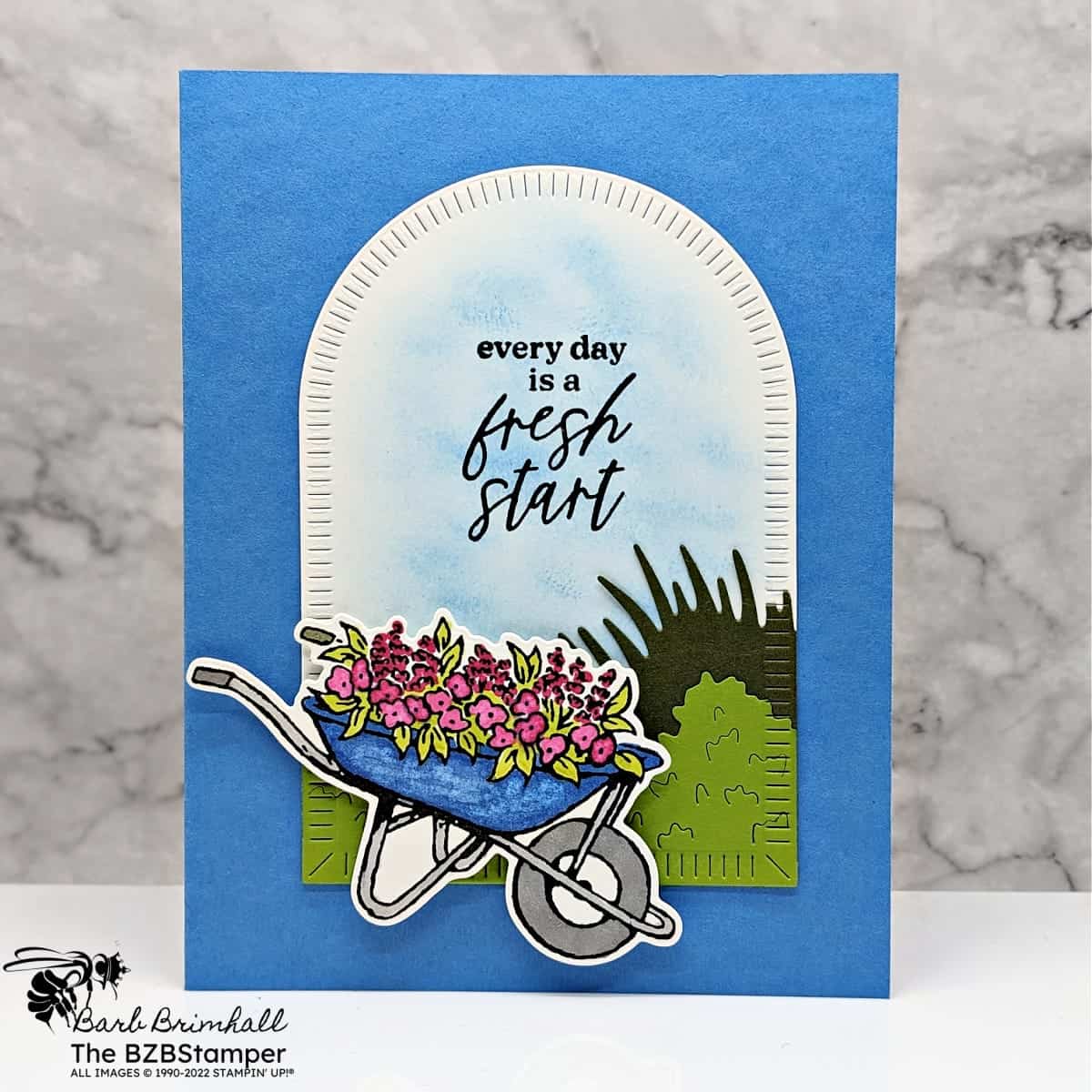 Garden Meadow All-Occasion Handmade Card 1 Handmade card in blues, greens and pinks featuring a wheelbarrow with flowers underneath an arch with sentiment "every day is a fresh start."