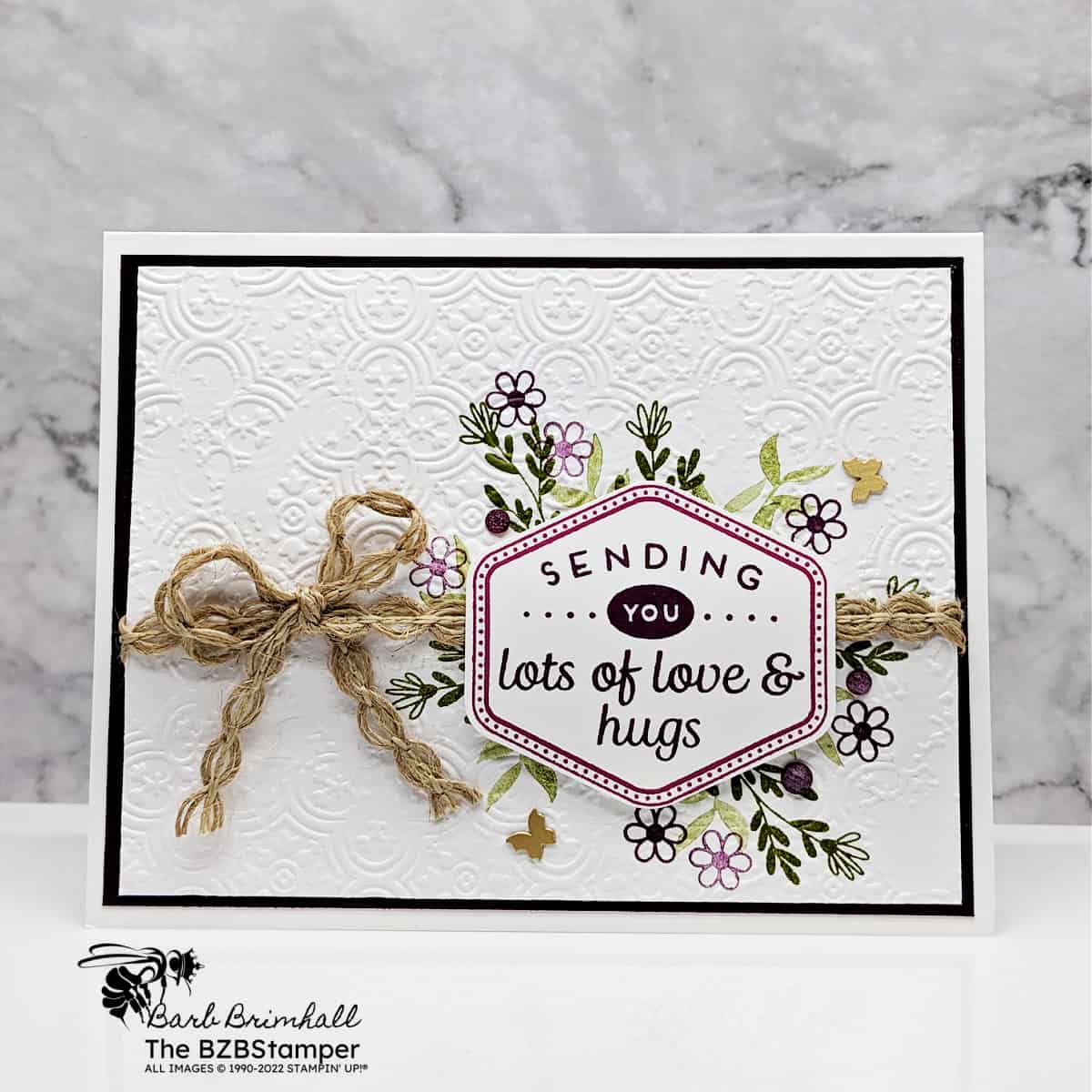 Handmade Thinking Of You Card Tutorial 1 Handmade Thinking Of You Card Tutorial featuring purple flowers and green foliage, with an embossed background. Sentiment is "sending you lots of love & hugs."