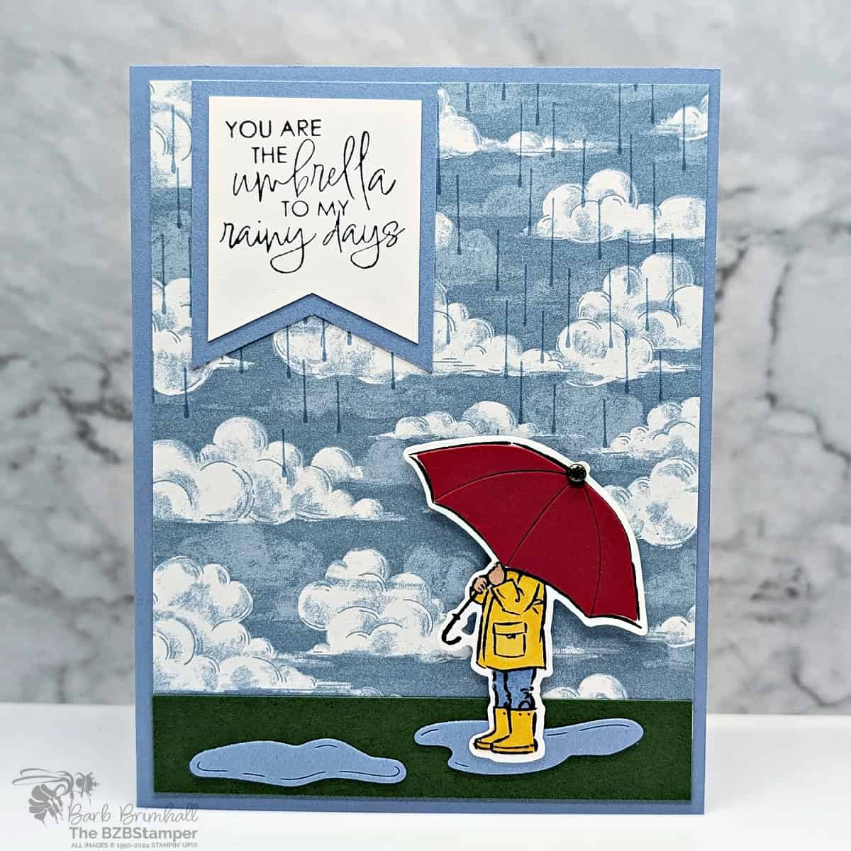 You Are the Umbrella to My Rainy Days 1 You Are the Umbrella to My Rainy Days handmade card featuring rainclouds and raindrops in blues and a person holding a red umbrella with the sentiment "you are the umbrella to my rainy days."