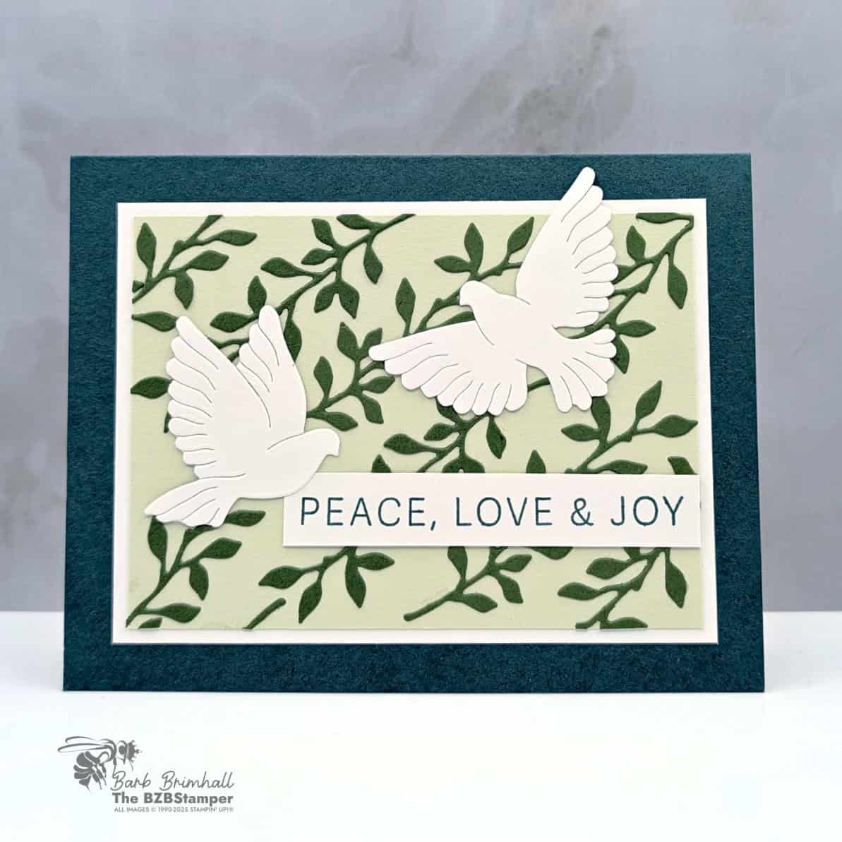 Peace On Earth Handmade Christmas Card Idea 1 Peace On Earth Handmade Christmas Card Idea featuring two white doves and the sentiment “Peace, Love & Joy,” with a leafy embossed background in Garden Green and Soft Sea Foam, framed by Pretty Peacock cardstock.