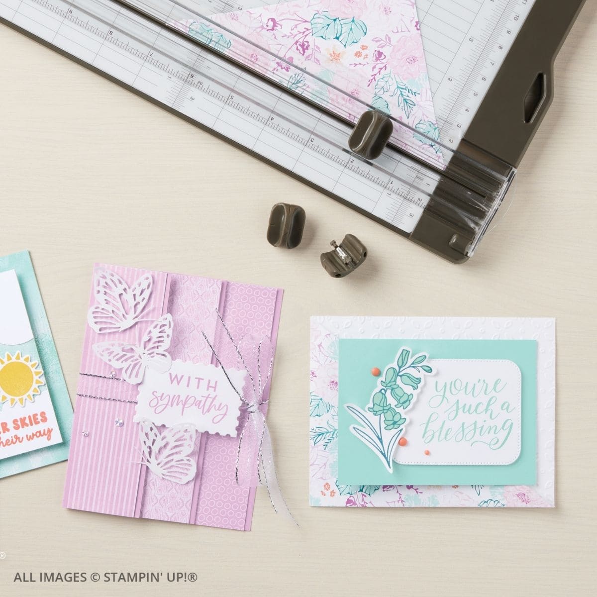 Building Relationships Through Cardmaking 2 Building Relationships Through Cardmaking. Two handmade cards in soft pastel tones featuring delicate stamped images and die-cut designs. One card says “With Sympathy” in pink and white, while the other says “You’re Such a Blessing” in mint and floral layers, surrounded by crafting tools and patterned paper.
